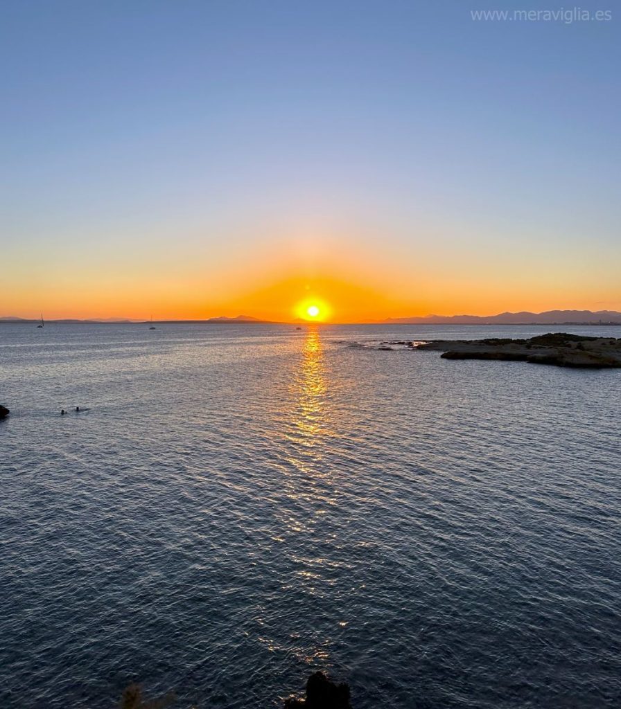El sol poniéndose en la costa alicantina, reflejando su luz en el mar y con un cielo anaranjado.