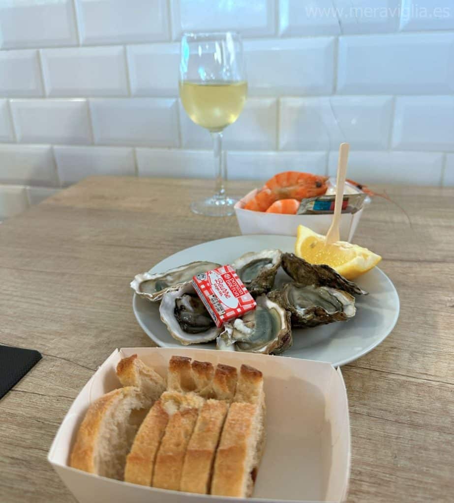 Plato de ostras de la bahía de Arcachon, bol con gambas, rebanadas de pan y copa de vino blanco.